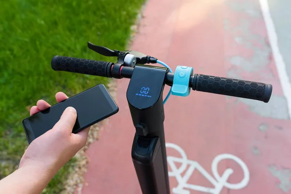 Parktaki bisiklet yolunda ekolojik bir scooter kullanan bir adamın elindeki telefon. Modern şehir yaşam tarzı.