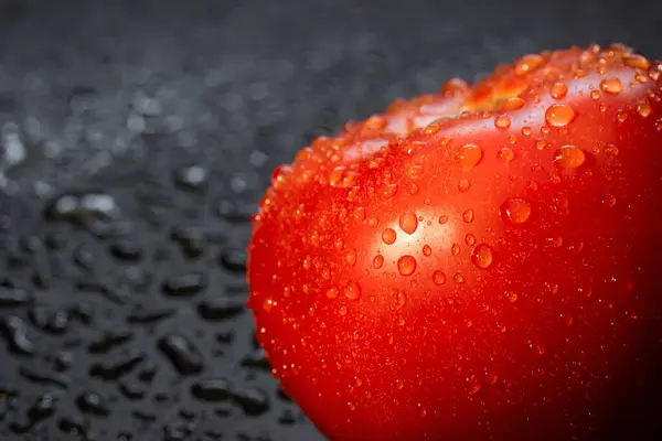 Ripe tomato with water drops on the table close-up.