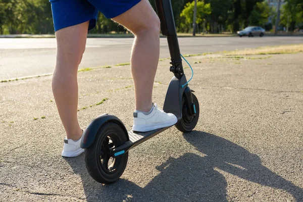 Yazın yolda elektrikli scooter kullanan bir adamın bacakları. Şehir taşımacılığı kavramı.