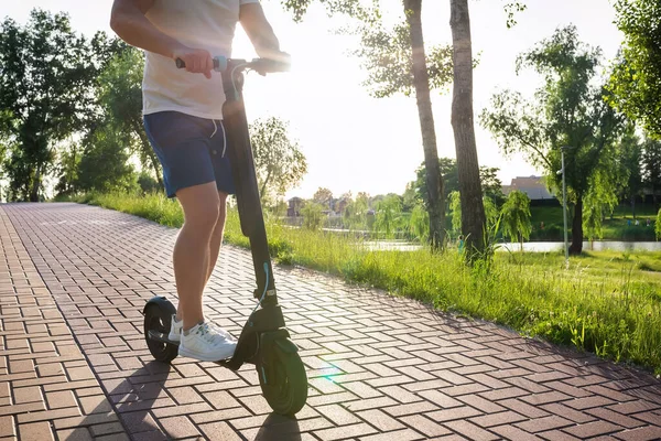 Parkta yolda elektrikli scooter süren genç bir adam..