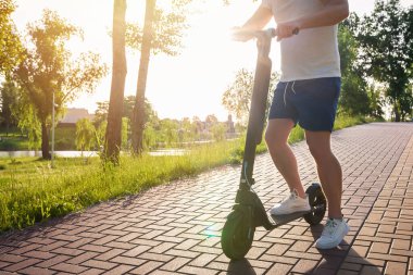 Güneşli bir günde, park yolunda, modern bir scooter kullanan bir adam. Kentsel yaşam tarzı, ekolojik ulaşım.