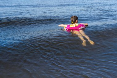 Şişme bir yüzükle denizde yüzen bir çocuk. Arka plan.