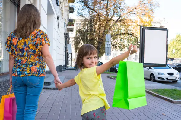 Mother and child on a street with shopping bags. Girl are holding the shopping bags.