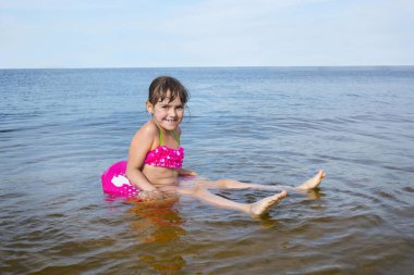 Küçük güzel bir kız, güneşli bir yaz gününde açık denizde şişme bir çemberde yüzer..