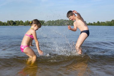 Çocuklar, sahil mevsiminde nehrin kıyısına su sıçratırlar. Çocuklarla yaz tatili.