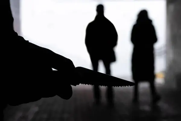 Karanlık bir tünelde arka planda bıçaklı bir adamın silueti. Şiddet, suç kavramı.