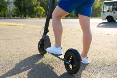 Güneşli bir günde şehirde bir adamın bacakları ve elektrikli scooter. Kentsel yaşam tarzı, ekolojik ulaşım.