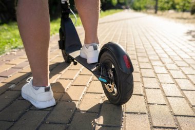 Parkta modern elektrikli scooter kullanan bir adam, yakın plan. Çevre dostu ulaşım.