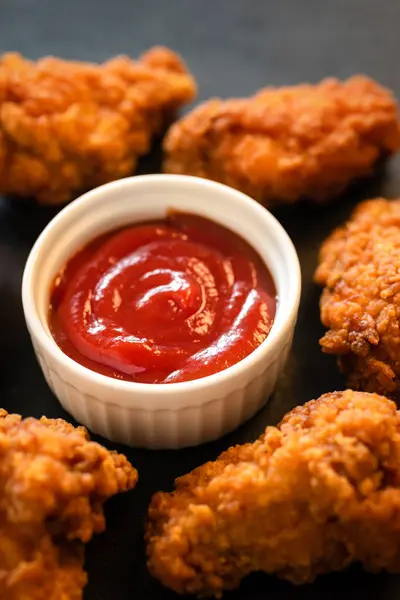 Crispy fried breaded chicken strips with red sauce on a dark background.