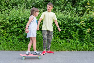 Kardeşiyle birlikte parkta kaykay süren küçük bir kız. Sağlıklı yaşam tarzı.