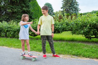 Mutlu çocuklar dışarıda parkta oynarlar. Bir oğlan kızına kaykay sürmeyi öğretiyor..