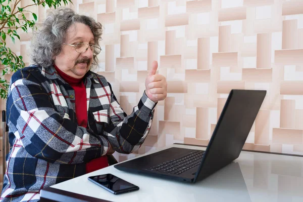An elderly man with a thumbs up is talking on a computer.