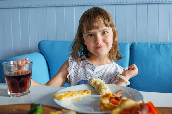 Çocuk bir kafede kahvaltı yapıyor ve kameraya poz veriyor. Fast food.