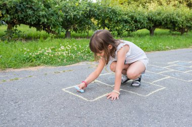 Küçük tatlı bir kız parktaki kaldırıma tebeşirle çiziyor..