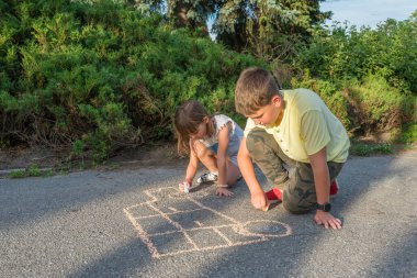 Çocuklar gün batımında parktaki kaldırıma tebeşirle çizer..