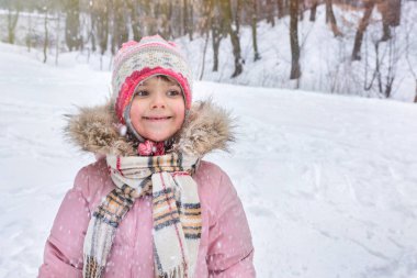 Kış giysileri içinde mutlu bir çocuk, kış yürüyüşü sırasında oynuyor ve gülümsüyor..