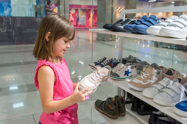 A little girl looks at shoes in a shopping center. Shopping.