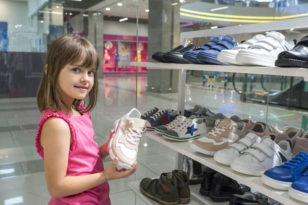 A little girl chooses sneakers in a store. Shopping, discounts.