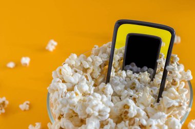 Sarı arka planda akıllı telefon ve patlamış mısır. Teknoloji konsepti. Patlamış mısırın arka planına sahip akıllı telefondaki sinema.