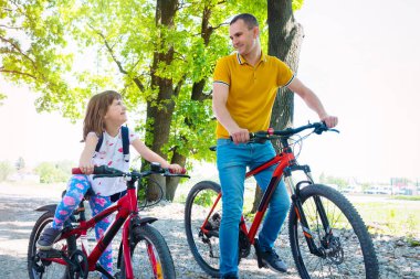 Mutlu bir baba ve kızı güneşli bir günde parkta bisiklete biniyor..