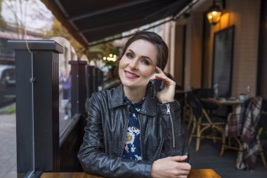 Şehir caddesinde, kafeteryanın terasında telefonla konuşan mutlu bir kız..
