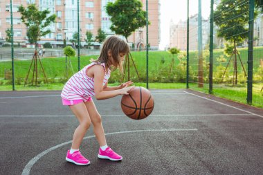 Bahçede elinde top olan bir kız basketbol oynuyor. Şehir dışında basketbol sahası.