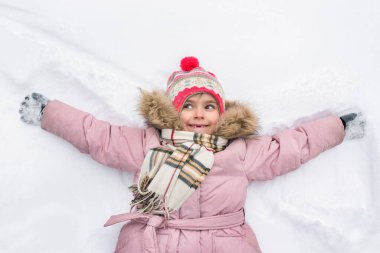 Çocuk bir melek şeklinde karın içinde uzanıyor. Pembe ceketli, kış parkında şaşırmış bir yüzü olan küçük kız..