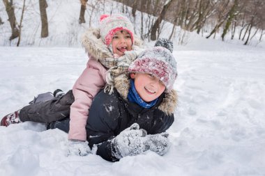 Kışlık giysili mutlu çocuklar dışarıda kar yığınında oynarken gülüyorlar. Kış çocukları tatilde..