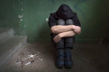 Terk edilmiş bir evde kollarını kavuşturmuş genç bir uyuşturucu bağımlısı. Uyuşturucu bağımlılığı ve depresyon krizi geçiren bir adam. Bağımlılık kavramı.