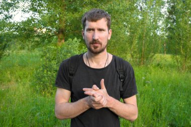 Arka planda yeşil ağaçlar olan bir ormanda açık havada sakallı bir adamın portresi..