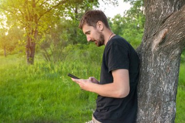 Ormanda elinde telefon olan genç bir adam. Parkta dinleniyor..