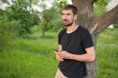 Güneşli bir günde ormanda elinde telefon olan genç bir adam. Etkin yaşam biçimi.