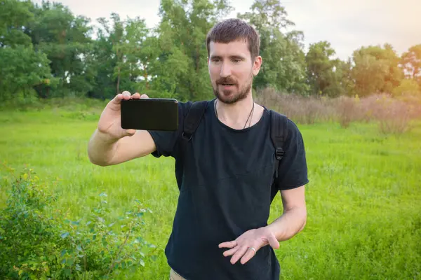 A male blogger is broadcasting in the forest on a mobile phone camera. Lifestyle, personal blog.