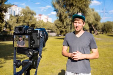 Adamın biri güneşli bir günde parkta kamerayla video blogu kaydediyor. Uzaklık yaşam tarzı kavramı