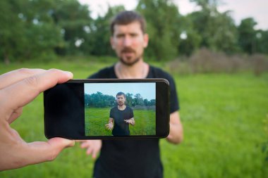 Genç bir adam parkta akıllı bir telefonla video blogu kaydediyor..