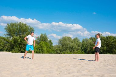 Kumsalda spor oyunları. Baba ve oğul kumsalda badminton oynuyorlar. Tatil, tatil, spor, yaşam tarzı.