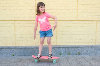 Kaykaylı modern şehirli hippi kız sarı duvarın arkasında eğleniyor..