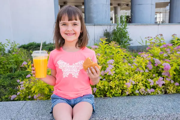 Happy girl with a hamburger and orange juice in her hands.