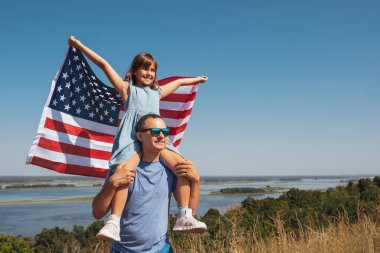 Mutlu aile babası ve kızı gün batımında Amerika bayrağıyla eğleniyor..