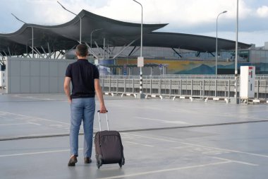 Açık bir otoparkta bavullu genç bir adam. Arkadan bak. Seyahat, tatil konsepti.