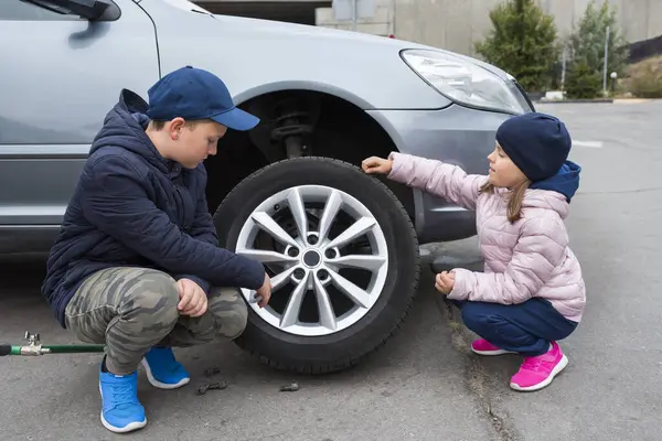 Children at the broken car, looking at the wheel. Car repair services.