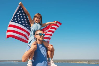 Mutlu aile babası ve kızı Amerika bayrağıyla babasının omuzlarında oturmuş doğanın tadını çıkarıyorlar. Özgürlük kavramı.