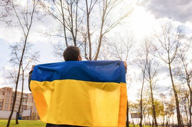 Ukrayna bayrağı taşıyan genç bir adam parktaki gökyüzüne bakıyor. Mavinin görüntüsü. Serbest yaşam biçimi.