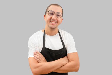 Siyah önlüklü genç adam gri arka plandaki kameraya bakıyor. Şef ya da garson konsepti..