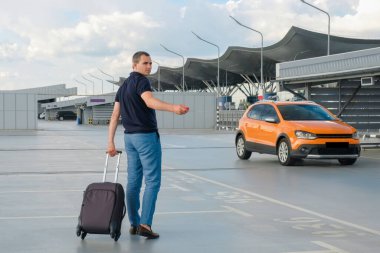 Elinde bavulu ve açık bir otoparkta uzaktan kumandalı araba anahtarı olan genç bir adam. Güvenlik kavramları