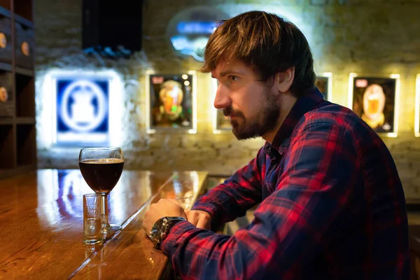 Lonely man in depression drinks an alcoholic beverage at the bar. A man in despair at the bar has alcohol addiction, alcoholism.