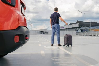 Araba parkında elinde bavul olan bir adamın arkası..