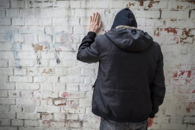 Kapüşonlu bir adam tuğla duvara karşı bağımlılık krizi yaşıyor. Arkadan manzara. Bağımlılık kavramı.