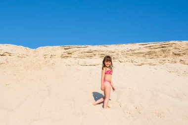 Güneşli bir günde kumlu bir plajda küçük bir kız. Dinlenme, tatil, aktif yaşam tarzı