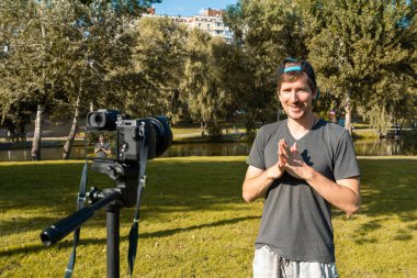 Genç adam parkta dijital kamerayla video kaydediyor. İş koçu, serbest çalışan, yaşam tarzı.